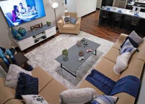 A Staged dorm living room with couches, TV, coffee table, white rug, and kitchen in the background